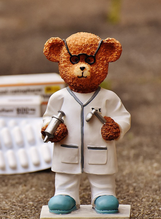 A porcelain bear, wearing doctor cloths and some tablets in blister packs in the background